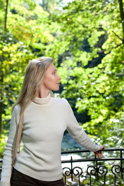 Die schöne Frau im weißen Pullover am Ufer des Sees vor leuchtend grünem Laub — Stockfoto