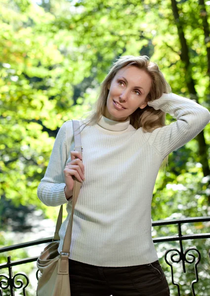 La bella donna in maglione bianco sulla riva del lago contro fogliame verde brillante — Foto Stock