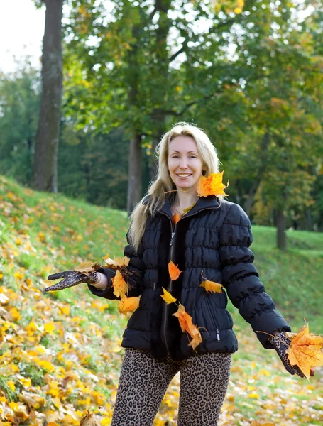 The beautiful woman in autumn park with an armful of maple leaves — Stock Photo, Image