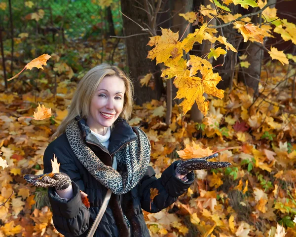 The beautiful woman in autumn park with an armful of maple leaves — Stock Photo, Image