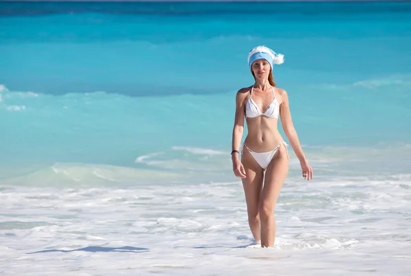 La giovane donna nel berretto dell'Anno nuovo cammina su una spiaggia — Foto Stock