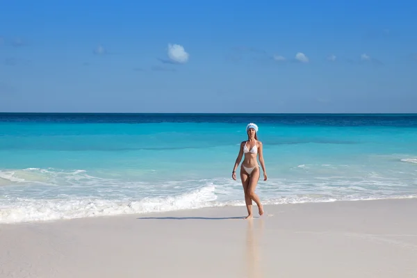 Die junge Frau mit der Neujahrsmütze spaziert am Strand — Stockfoto