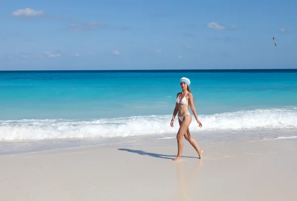 A jovem mulher no gorro do Ano Novo caminha em uma praia — Fotografia de Stock