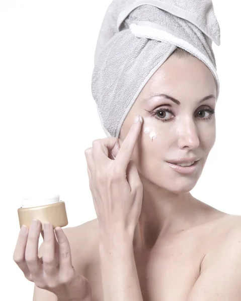 De mooie jonge vrouw in de handdoek met een cosmetische crème — Stockfoto