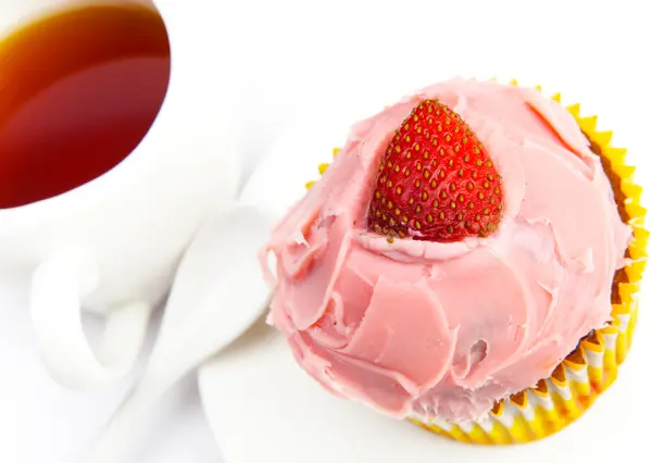 Bolo de frutas com um morango e uma xícara de chá — Fotografia de Stock