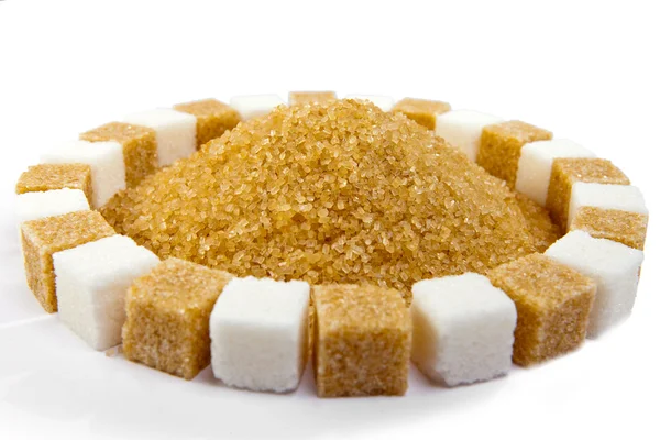 Cubes of sugar lie on circles and candy sugar on a stick on a heap of granulated sugar inside — Stock Photo, Image