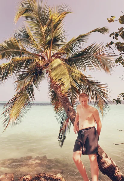 Teenager at palm tree and ocean in the background, with a retro effect — стоковое фото