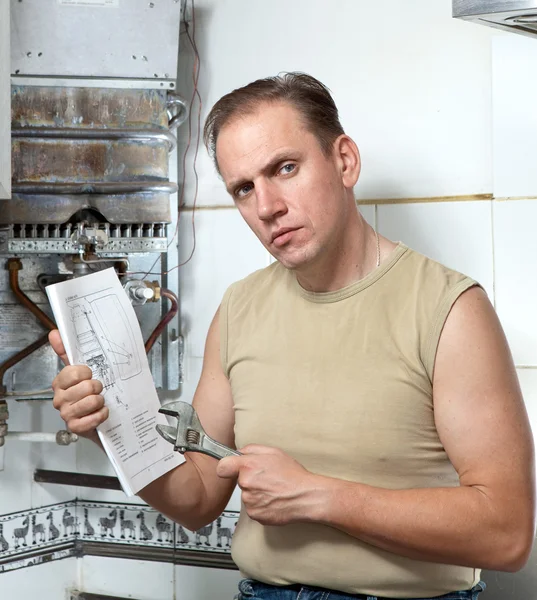 Der Mann mit dem Schraubenschlüssel sieht die Anleitung zur Reparatur eines Gas-Warmwasserbereiters — Stockfoto