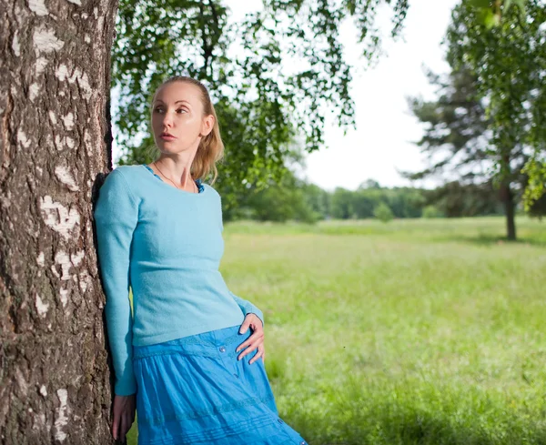 Die schöne junge Frau im blauen Kleid auf dem Feld an der Birke — Stockfoto