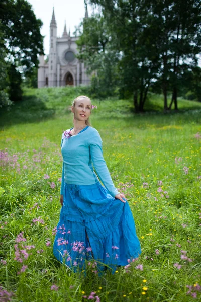 De mooie jonge vrouw in een blauwe jurk in het veld op een oud kasteel — Stockfoto