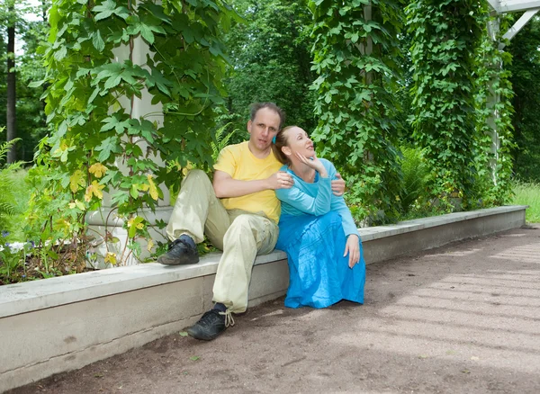 Young happy couple sits in the arbour twined greens — Stock Photo, Image