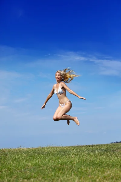 Onnellinen nainen hyppää vihreällä pellolla sinistä taivasta vasten. — kuvapankkivalokuva
