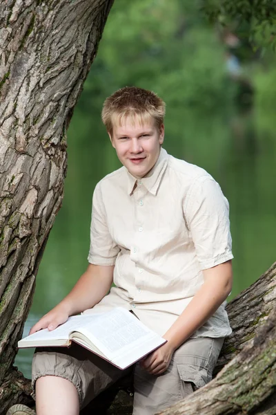 O jovem com o livro no parque na margem do lago — Fotografia de Stock