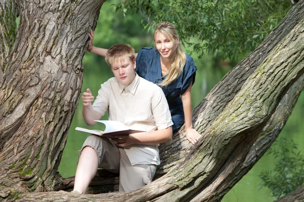Ung kille och flickan förbereda lektioner, undersökning i vår park nära lake — Stockfoto