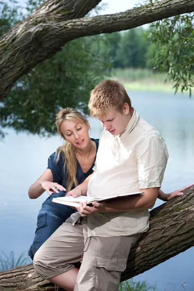 Young guy and the girl prepare for lessons, examination in spring park near lake — Stock Photo, Image