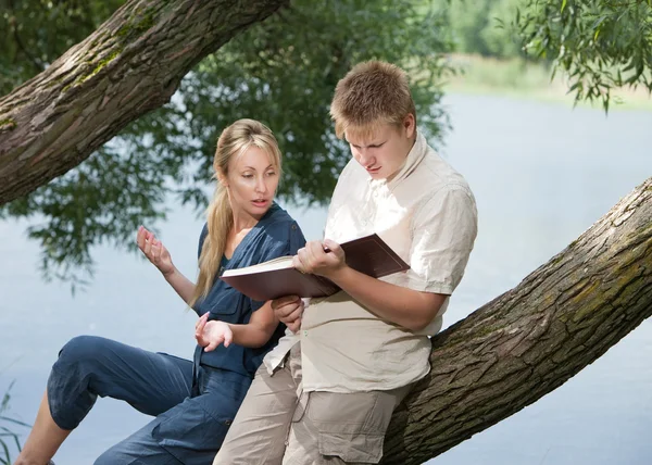 Joven chico y la chica se preparan para las lecciones, examen en el parque de primavera cerca del lago —  Fotos de Stock