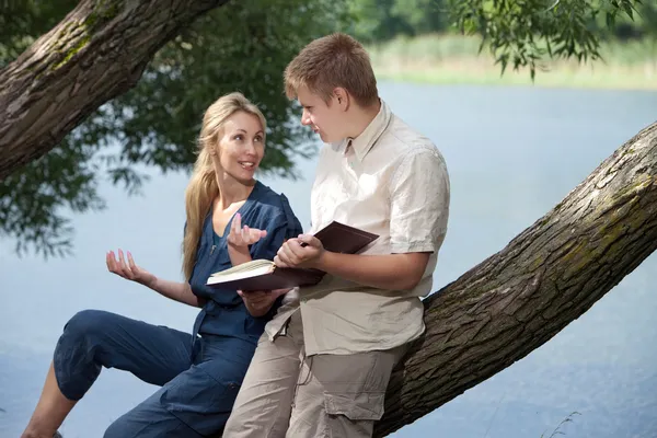 Jovem e a menina com livros na margem do lago — Fotografia de Stock