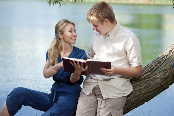 Young guy and the girl with textbooks on the bank of lake — Stock Photo, Image