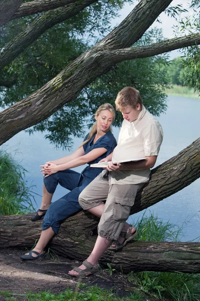 Jovem e a menina com livros na margem do lago — Fotografia de Stock