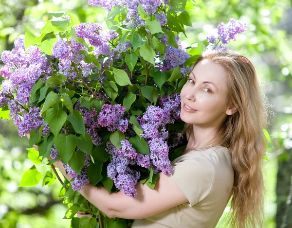 Glückliche junge Frau im Park mit einem großen Strauß Flieder — Stockfoto