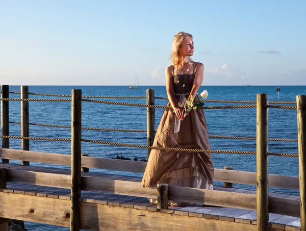 海の上の木製の道路上の長いドレスの若い美しい女性 — ストック写真
