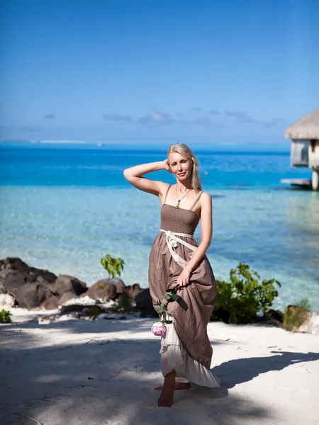 The young beautiful woman in a romantic dress with a rose on sand at the sea edg — Stock Photo, Image