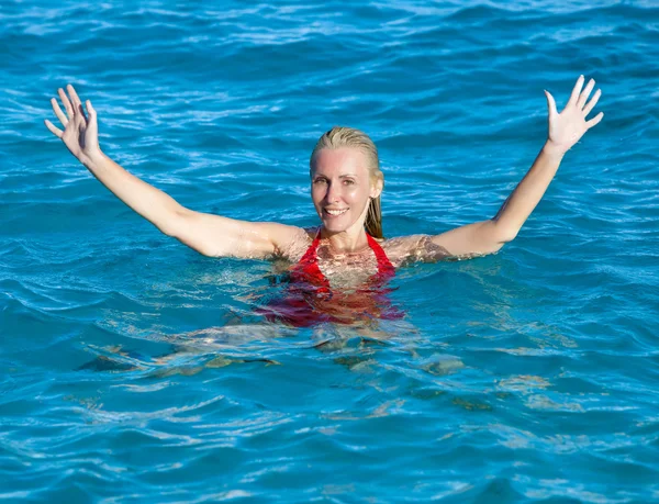 The happy woman in the sea waves to us greeting a hand — Stock Photo, Image