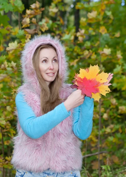 The beautiful woman in autumn park with an armful of maple leaves — Stock Photo, Image