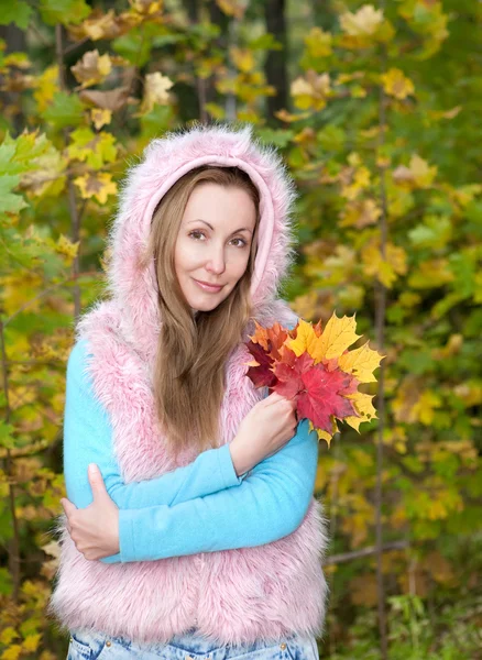 Die schöne Frau im Herbstpark mit einem Arm voller Ahornblätter — Stockfoto