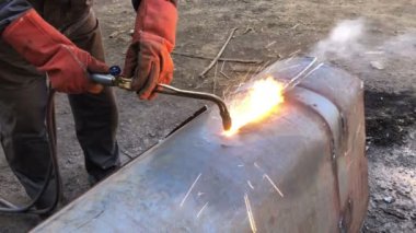 Kaynakçı büyük metal boruları seketilen kaynakla keser. Sokakta çalışan bir işçi gündüzleri büyük çaplı borular kesiyor ve kıvılcımlar ve ateş uçuşuyor..