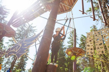 Macera parkında güvenlik ekipmanı içinde küçük bir kız. Çocuk dışarıda eğleniyor. Çocukluk sporları ekstrem aktiviteler. Yaz ışığı.