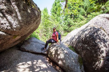Kayaların üzerinde oturan mutlu kadın yürüyüşçü portresi. Yaz günü. Doğadaki macera.
