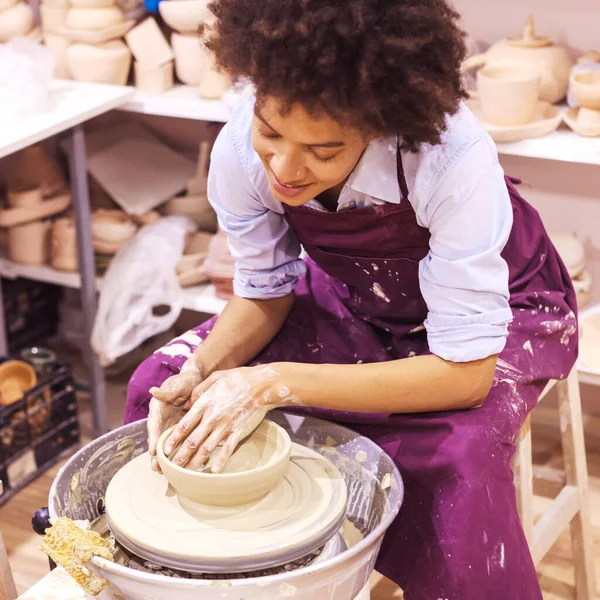 Creative afro american young woman molding clay on pottery wheel. Workshop in ceramic studio.