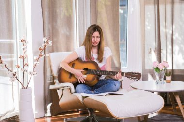 Evde gitar çalan genç bir kadın. Müzik aleti çalmayı öğreniyorum. Boş zaman hobisi.
