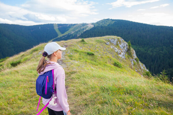 Little girl with backpack admire amazing view, beautiful summer day, mountain nature landscape.Children activity.
