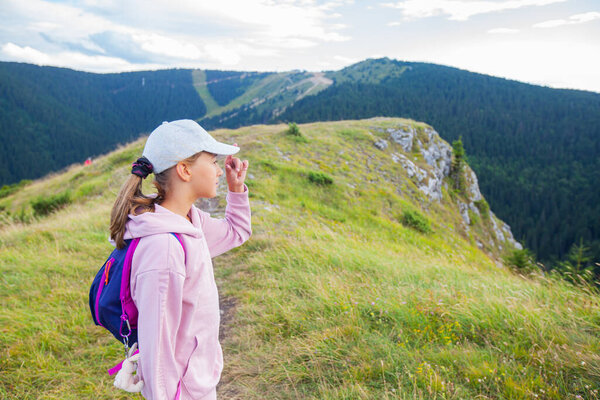 Little girl with backpack admire amazing view, beautiful summer day, mountain nature landscape.Children activity.