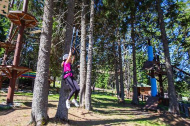 Çocuk macera eğlence parkında güvenlik ekipmanı kullanıyor. Genç kız dışarıda eğleniyor. Çocukluk aktif. Aşırı spor faaliyetleri.