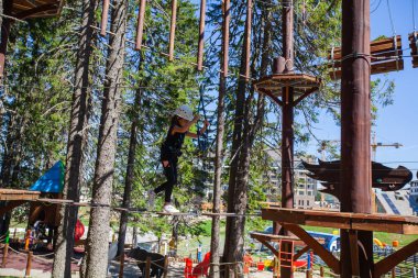 Çocuk macera eğlence parkında güvenlik ekipmanı kullanıyor. Genç kız dışarıda eğleniyor. Çocukluk aktif. Aşırı spor faaliyetleri.