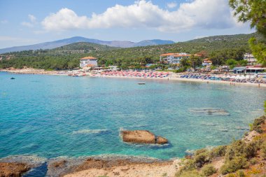 Körfezdeki güzel sahil manzarası. Açık turkuaz renk denizi. Çam ormanları sahil şeridini sarar. Güneşli yatakları ve güneşliği olan organize plajlar. Yaz tatili.