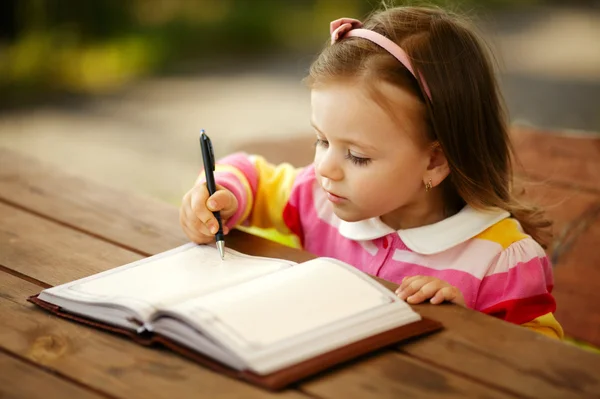 Little girl writes to the notepad — Stock Photo, Image