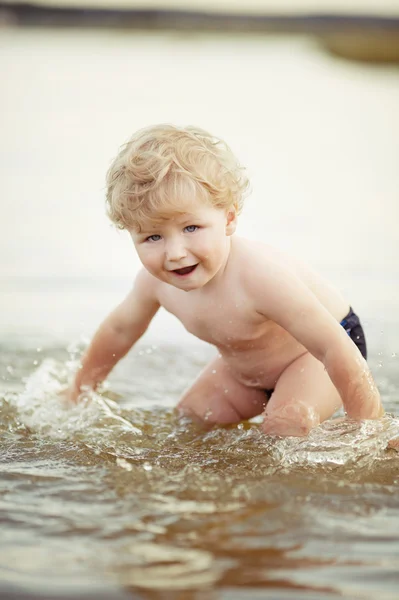 Маленький забавный мальчик играет в озере — стоковое фото