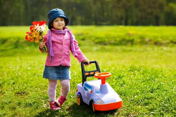 Kleines Mädchen mit Spielzeugauto und Blumen — Stockfoto