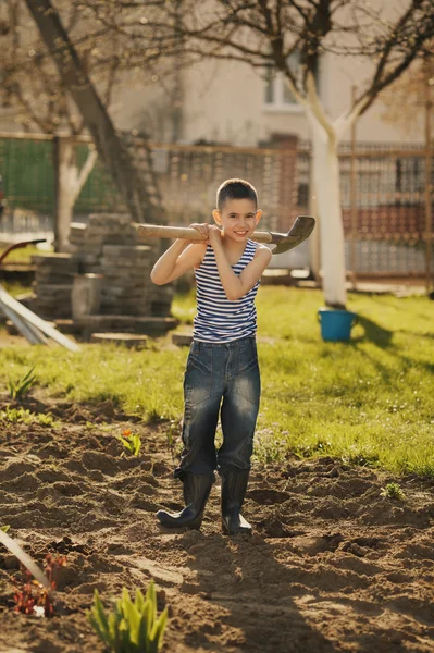 Маленький мальчик работает с лопатой в саду — стоковое фото