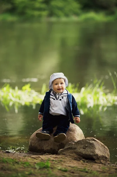 Kleine jongen zittend op grote steen in de buurt van water — Stockfoto