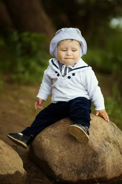 Маленький мальчик сидит на большом камне возле воды — стоковое фото