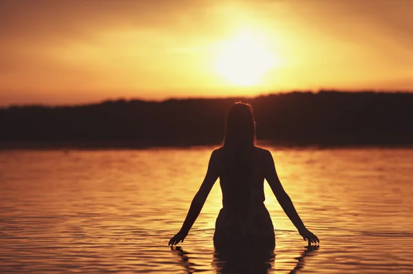 Hermosa chica en el agua en la puesta del sol — Foto de Stock