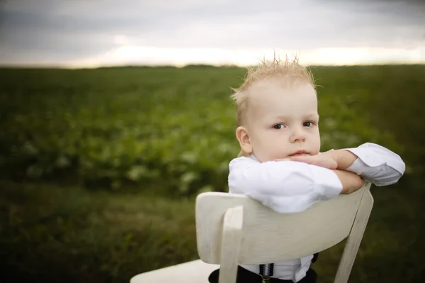 Мальчик сидит на стуле в поле — стоковое фото