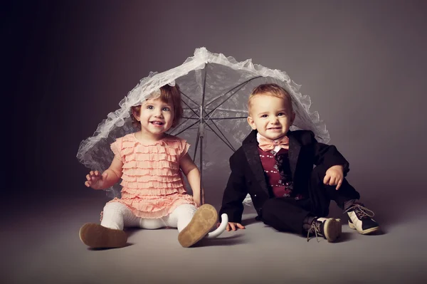 Маленький веселый мальчик и девочка под зонтиком — стоковое фото