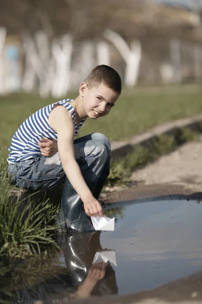 Little boy plays with paper boats in puddle — Stock Photo, Image