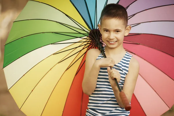 Happy boy with a rainbow umbrella in park — Stock Photo, Image